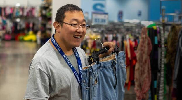 goodwill employee holds up pair of jeans at a store