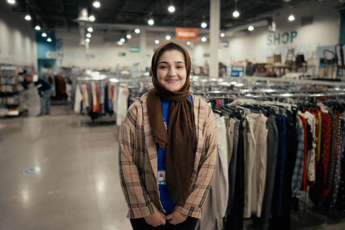 woman in traditional head scarf smiles at camera, wearing a goodwill shirt