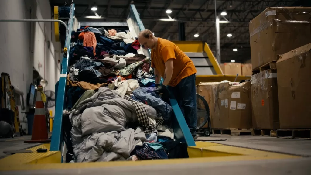 man in orange t-shirt sorts through clothes on conveyer belt